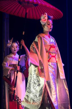 Geleneksel Japon gösterisi. Geleneksel kimono ve tilki damgalı aktris yavaş yavaş gidiyor ve asistanı şemsiyeyi başının üstünde tutuyor..