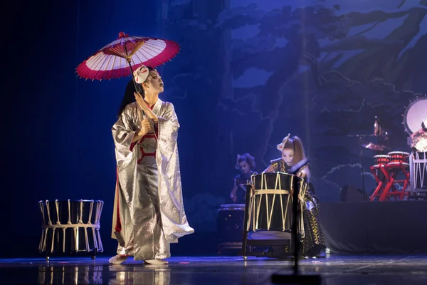 Traditional Japanese performance. Actress in traditional kimono on the dark stage with umbrella and taiko drummers.