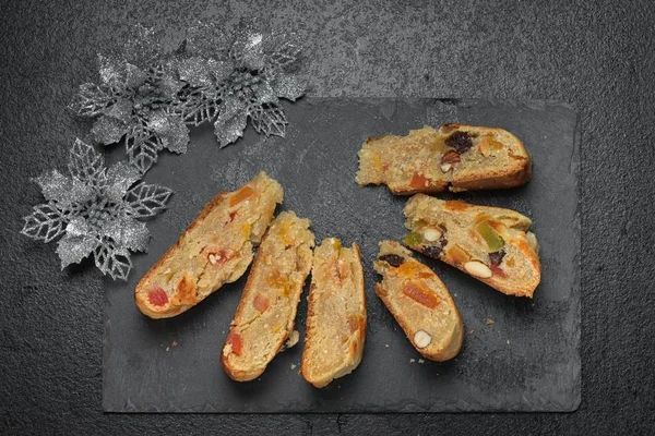 Stollen traditional Christmas cake made in a round cooker, on a black stone board background with christmas decorations, top view.