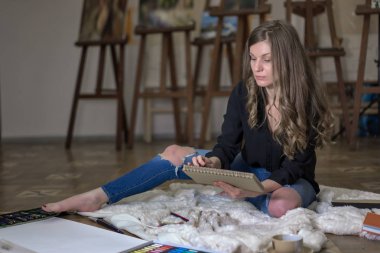 Resim stüdyosundaki sanatçı yere oturmuş resim çiziyor..