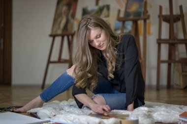 Resim stüdyosundaki sanatçı yere oturmuş resim çiziyor..