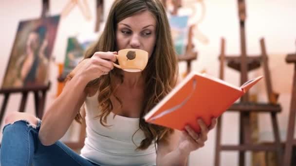 Mujer artista bebiendo café y pintura cuadro sentado en su elegante taller — Vídeos de Stock