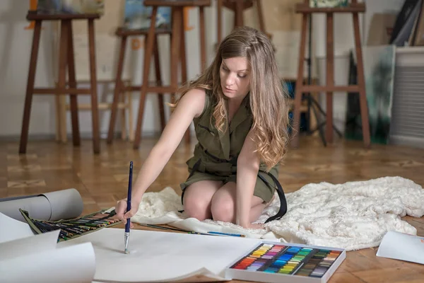 Artist woman sits on the floor and paints in art studio. Copy space on the paper for your text.