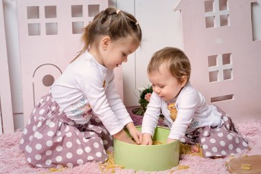 İki kız kardeş. 1 ve 3 yaşlarındaki kızlar mutfakta yerde oturup kuru makarnayla oynuyorlar..