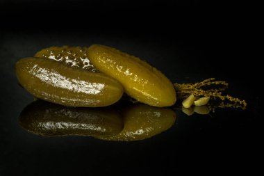 Siyah ayna yüzeyinde sarımsak ve tarhun salatalık turşusu. Siyah arka planda yansımaları var.