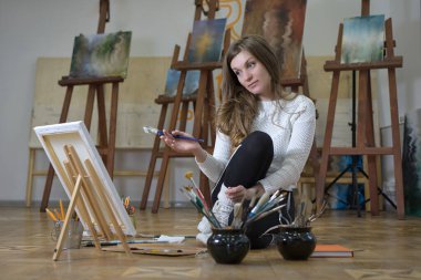 Kadın sanatçı bir sanat stüdyosunda yerde oturur ve yağlı boya tablolarını tuvale çizer..