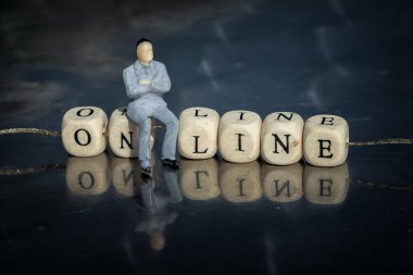 Online bir küpün üzerinde, üzerinde harfler olan, ipliğe sarılı bir metin olarak oturan iş adamının minyatür modeli. Çevrimiçi iş kavramı.