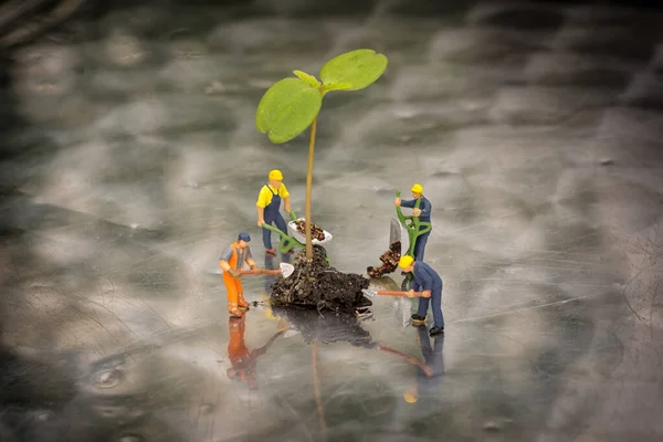 Miniiature people planting a tree.