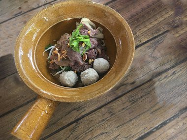 Ahşap bir masaya konmuş kil bir kasede kurutulmuş et ve köfte.