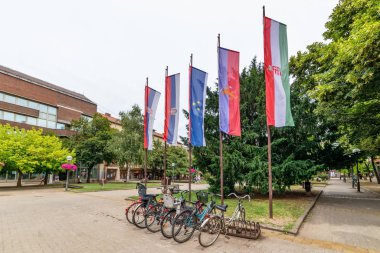 Kikinda, Sırbistan - 26 Temmuz 2019: Kikinda belediye binasının önünde bayraklar ve park edilmiş bisikletler.
