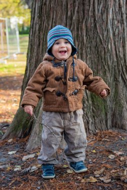 Sonbahar parkında duran küçük çocuk. Sopalı çocuk.