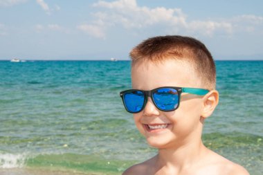 Sahilde güneş gözlükleriyle poz veren güzel bir çocuk.