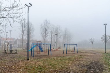 Novi Sad, Sırbistan - 16 Ocak 2020: Sis dolu çocuk parkı. Sisli parkta atlıkarıncalı ve salıncaklı boş oyun alanı.