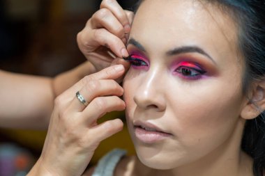 Makyöz takma kirpik takıyor. Makyaj sanatçısı, genç ve güzel bir kadının profesyonel makyajını yapıyor.. 