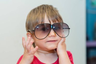 Büyük güneş gözlüklü küçük çocuk. Yüzünde kocaman güneş gözlüğü takan sevimli bir çocuğun resmi var.