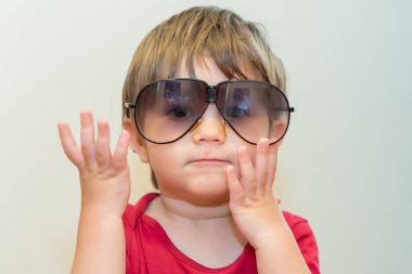 Büyük güneş gözlüklü küçük çocuk. Yüzünde kocaman güneş gözlüğü takan sevimli bir çocuğun resmi var.
