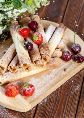 Kremalı gözlemeler, kirazlarla süslenmiş çilekler, üzerine pudra şekeri serpiştirilmiş ev yapımı kekler.