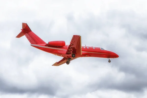 Overhead view of a red business jet airplane short before landing. Overcast, cloudy sky. — Stock Photo, Image