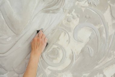 İşteki kadın, zımpara kağıdıyla duvardaki kabartmaları hallediyor.