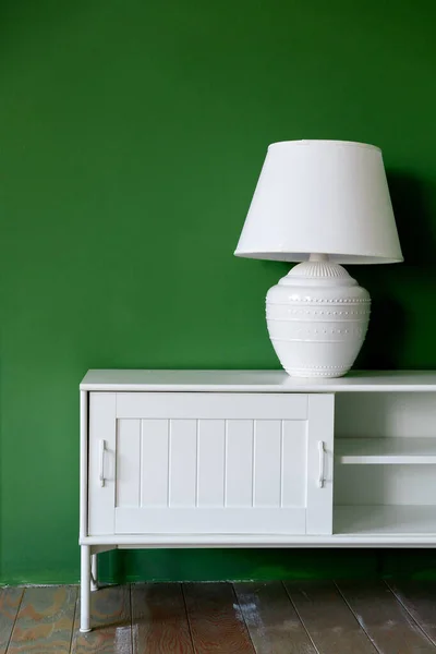 Beyaz lamba beyaz bir kaidede yeşil bir duvara karşı — Stok fotoğraf