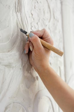 İş akışını onar, keski aletli bir kadın duvara kabartma deseni oyar.