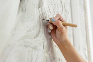 Çalışma akışı, keski aletli bir kadın duvara kabartma deseni oyuyor.