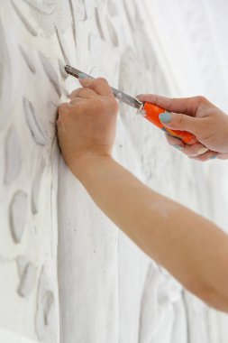 İşyerindeki bir kadın, elinde keski ile duvara kabartma deseni kazıyor.