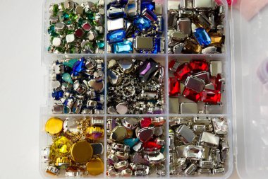 Beyaz ahşap arka plandaki bir kapta farklı renkte, şekillerde, boyutlarda boncuklar ve cam boncuklar var.