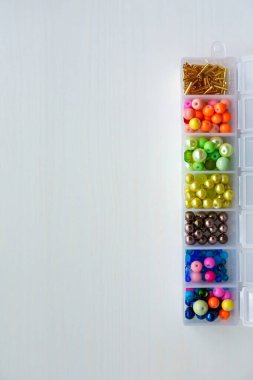 Beyaz ahşap arka plandaki bir kapta farklı renkte, şekillerde, boyutlarda boncuklar ve cam boncuklar var.