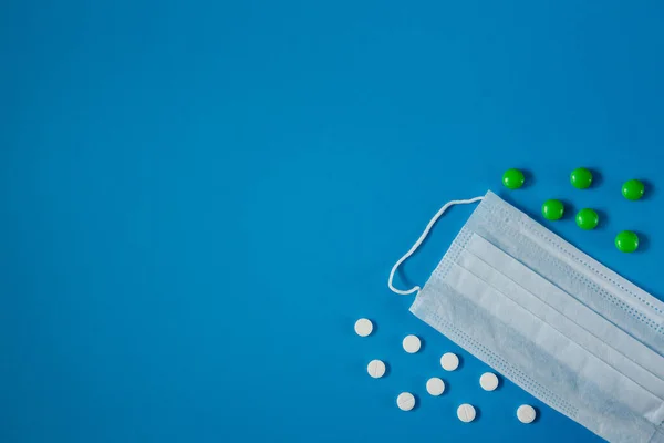 medical mask on the face and white and green pills, on a blue background from above in the corner