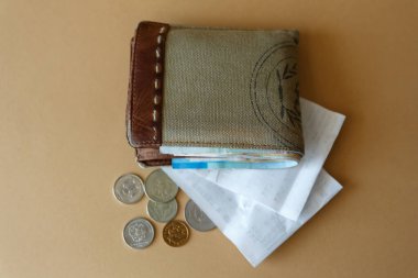 Cüzdanında para, bozuk para ve arka planda düz ışık olan bir kasiyer çeki var. Satın alma maliyetleri ve hizmetler için ödeme.