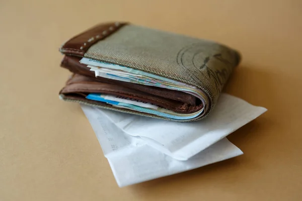 Side view of a wallet with money and a cashier\'s check from the store on a plain light background. Costs of purchases and payment for services.