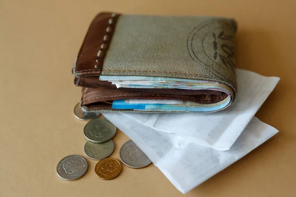 Wallet with money, coins and a cashiers check from the store on a plain light background, side view. Costs of purchases and payment for services.