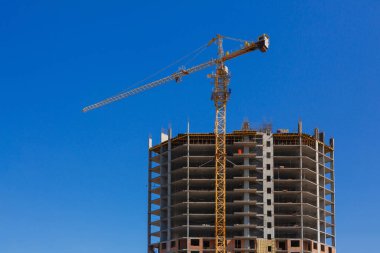 İnşaat vinci. Mavi gökyüzüne karşı yüksek bir bina yapım aşamasında. İnşaat endüstrisi ve sanayi