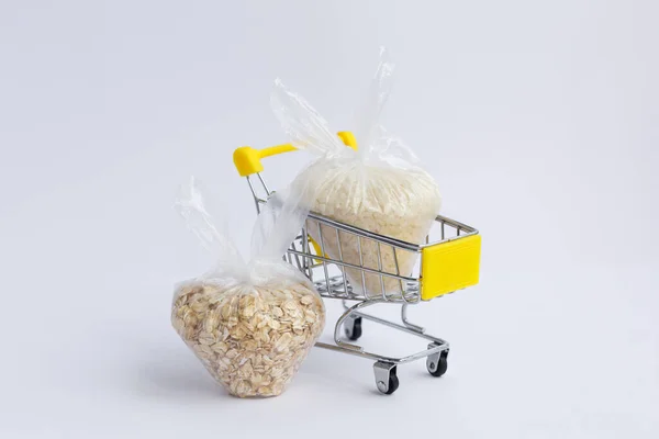 various groats in packages in a grocery cart on a white background. Rice and oatmeal