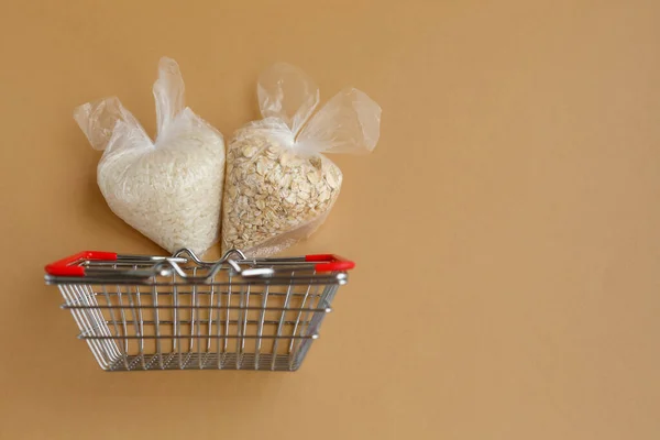 various groats in packages in a grocery basket on a brown background. Rice and oatmeal