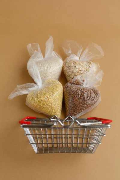 various groats in packages in a grocery basket on a brown background. Rice and oatmeal, buckwheat and millet