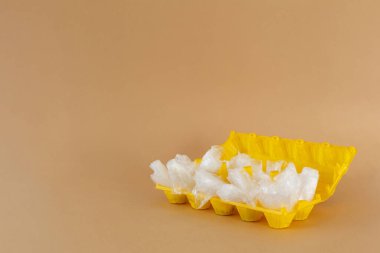 Kahverengi arka planda sarı plastik bir yumurta kabında şeffaf plastik torbalar. Ekoloji ve çöp.