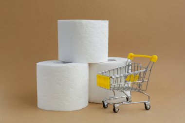 Beyaz arka planda üç rulo beyaz tuvalet kağıdı ve küçük bir market arabası.