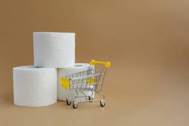 Beyaz arka planda üç rulo beyaz tuvalet kağıdı ve küçük bir market arabası.