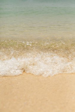 Dalgada parla. Okyanusun sarı kumlu tabanı. Deniz köpüğü ve dalgalar kıyıya vuruyor.