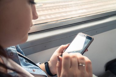 Genç, güzel, beyaz bir kız yolculuk sırasında toplu taşıma araçlarında akıllı telefon kullanıyor.