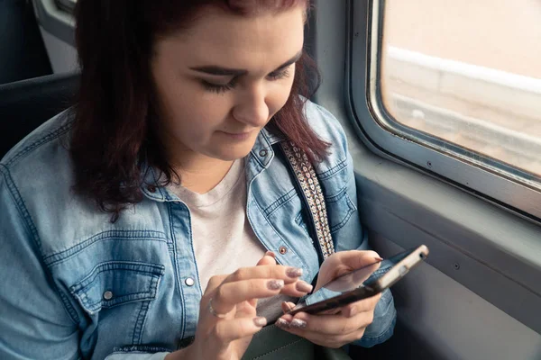 Genç, güzel, beyaz bir kız yolculuk sırasında toplu taşıma araçlarında akıllı telefon kullanıyor.
