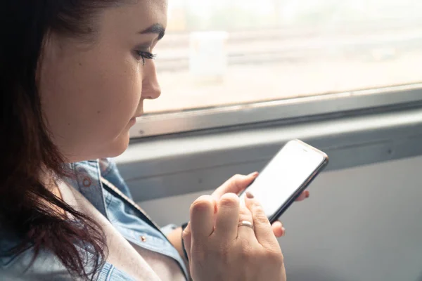 Genç, güzel, beyaz bir kız yolculuk sırasında toplu taşıma araçlarında akıllı telefon kullanıyor.
