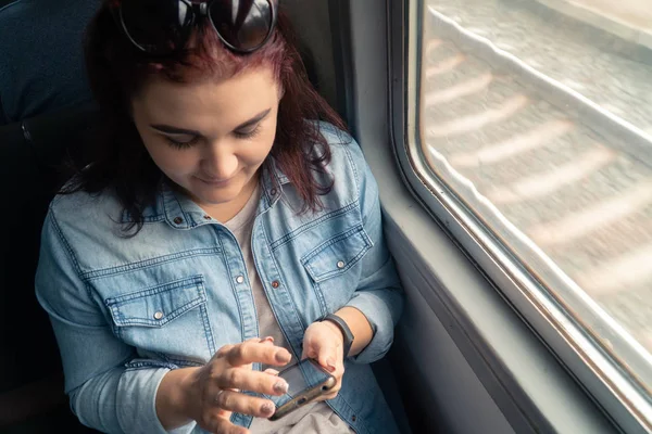 Genç, güzel, beyaz bir kız yolculuk sırasında toplu taşıma araçlarında akıllı telefon kullanıyor.