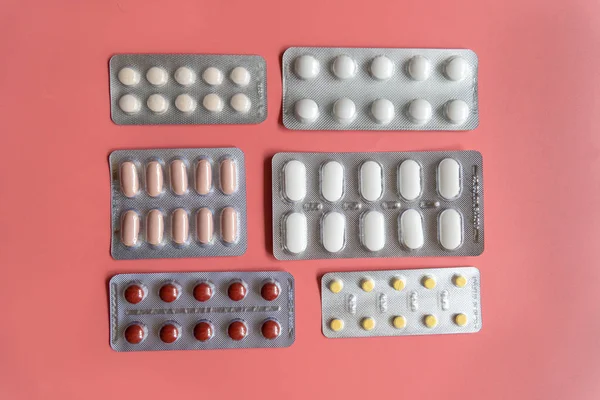 Verschillende blisterverpakkingen met tabletten op roze achtergrond — Stockfoto