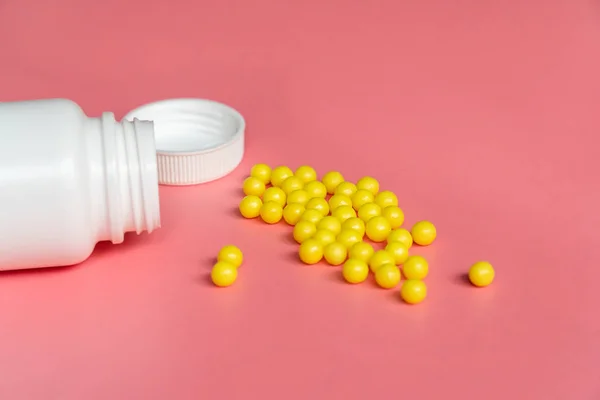 Żółta okrągła tabletka lub kapsułka na różowym tle z przestrzenią do kopiowania przy białym plastikowym zbliżeniu butelki — Zdjęcie stockowe