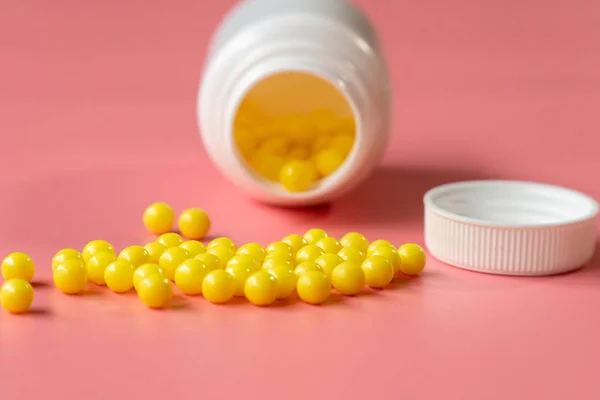 Κίτρινο στρογγυλό χάπι ή κάψουλα σε ροζ φόντο με αντίγραφο χώρο δίπλα σε ένα λευκό πλαστικό μπουκάλι close-up — Φωτογραφία Αρχείου