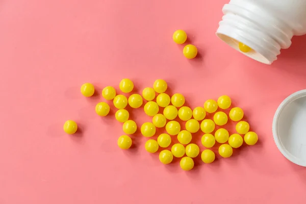 Żółta okrągła tabletka lub kapsułka na różowym tle z przestrzenią do kopiowania przy białym plastikowym zbliżeniu butelki — Zdjęcie stockowe