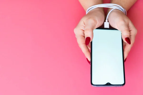 Vista dall'alto le mani della donna hanno uno smartphone moderno con schermo bianco su sfondo rosa. Dipendenza da siti di social networking, internet e gadget  . Immagine Stock